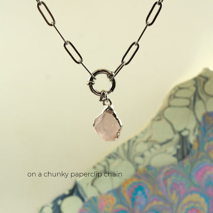 A silver paperclip chain necklace with a circular ring connector and a small faceted pale pink raw rose quartz gemstone pendant