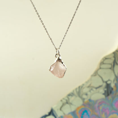 A delicate silver chain necklace with a small, irregular faceted pale pink rose quartz gemstone pendant