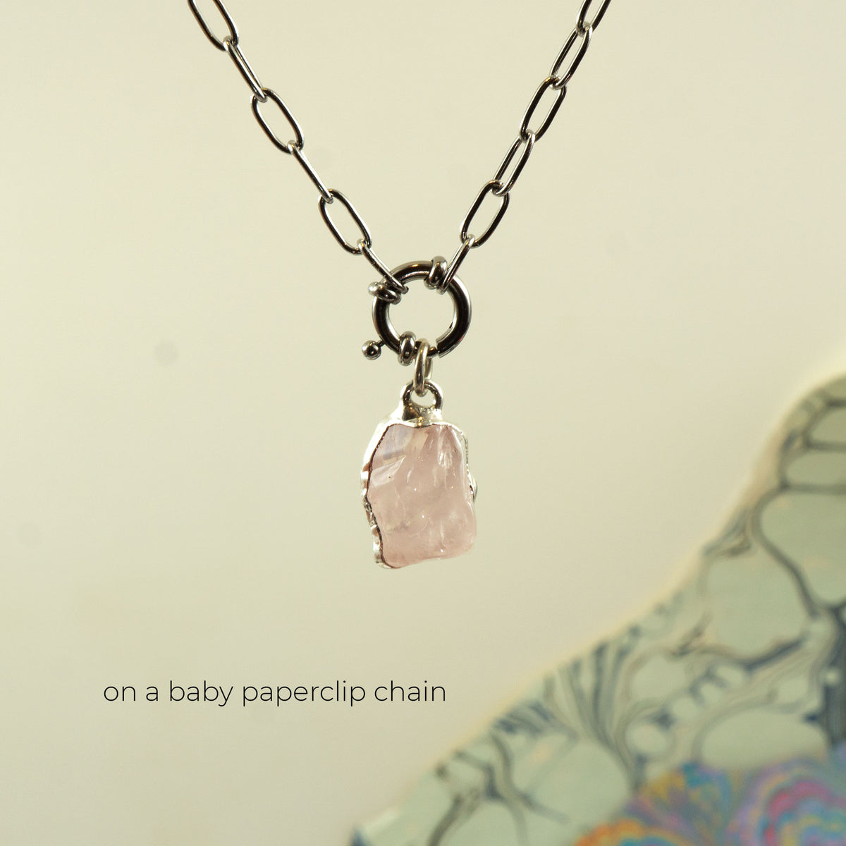 A silver paperclip chain necklace with a ring clasp holding a raw, irregular-cut pale rose quartz pink stone pendant