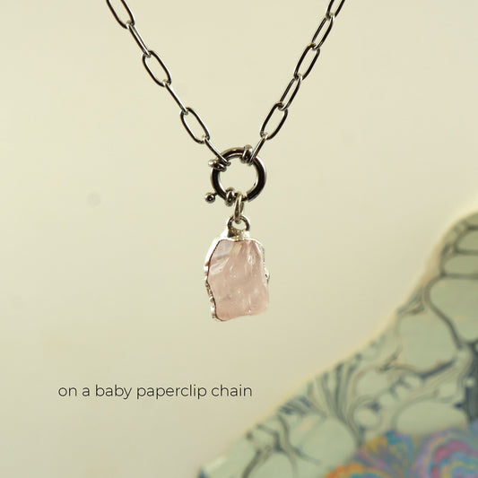 A silver paperclip chain necklace with a ring clasp holding a raw, irregular-cut pale rose quartz pink stone pendant