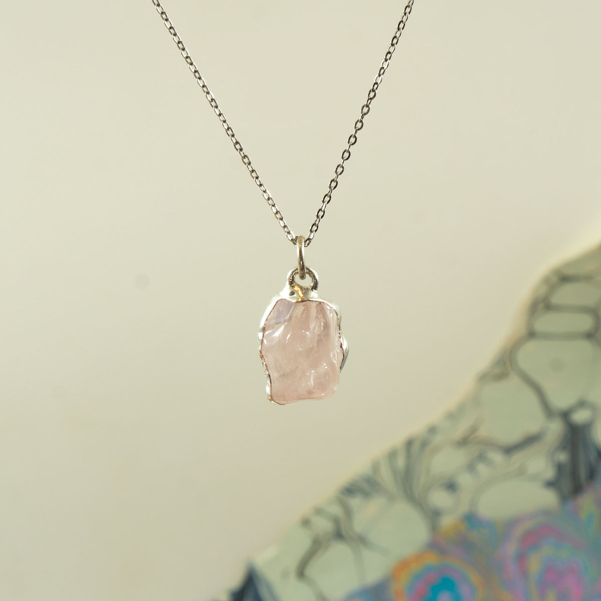 A delicate silver chain necklace with a raw, faceted pink rose-quartz stone pendant