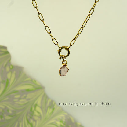 A gold paperclip chain necklace with a small gold clasp holding a light pink raw stone pendant