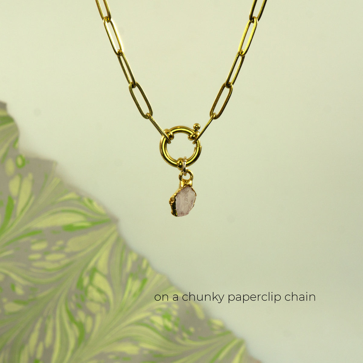 A gold paperclip chain necklace with a ring clasp and a small raw, irregular pink stone pendant
