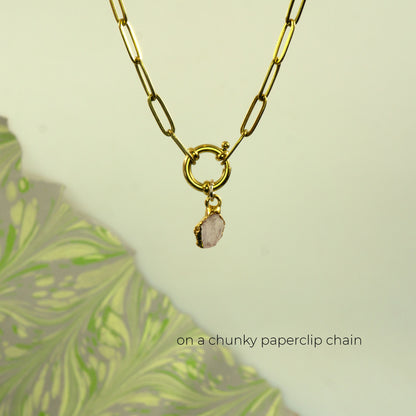 A gold paperclip chain necklace with a ring clasp and a small raw, irregular pink stone pendant