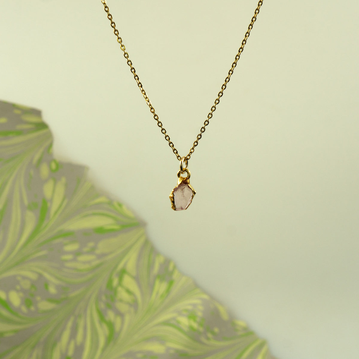 A delicate gold chain necklace with a raw, irregular pink stone pendant