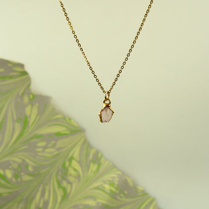 A delicate gold chain necklace with a raw, irregular pink stone pendant