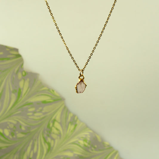A delicate gold chain necklace with a raw, irregular pink stone pendant