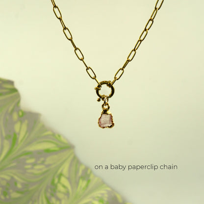 A gold paperclip chain necklace with a small gold clasp and a dangling light rose quartz stone charm