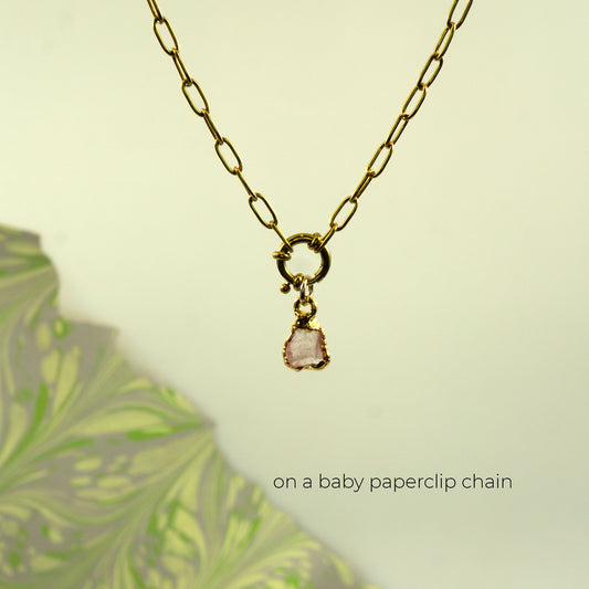 A gold paperclip chain necklace with a small gold clasp and a dangling light rose quartz stone charm