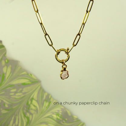 A gold paperclip chain necklace with a small ring pendant and a small dangling raw rose quartz stone
