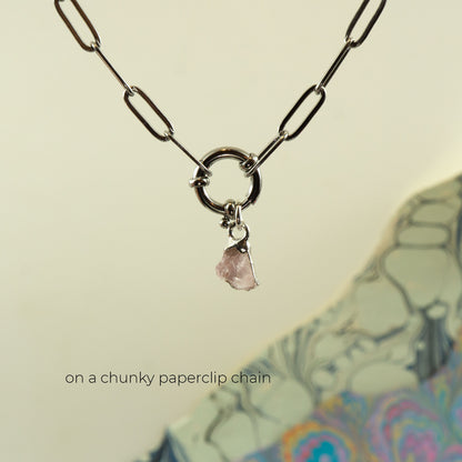 A silver paperclip chain necklace with a circular ring clasp and a small pink rose quartz stone charm