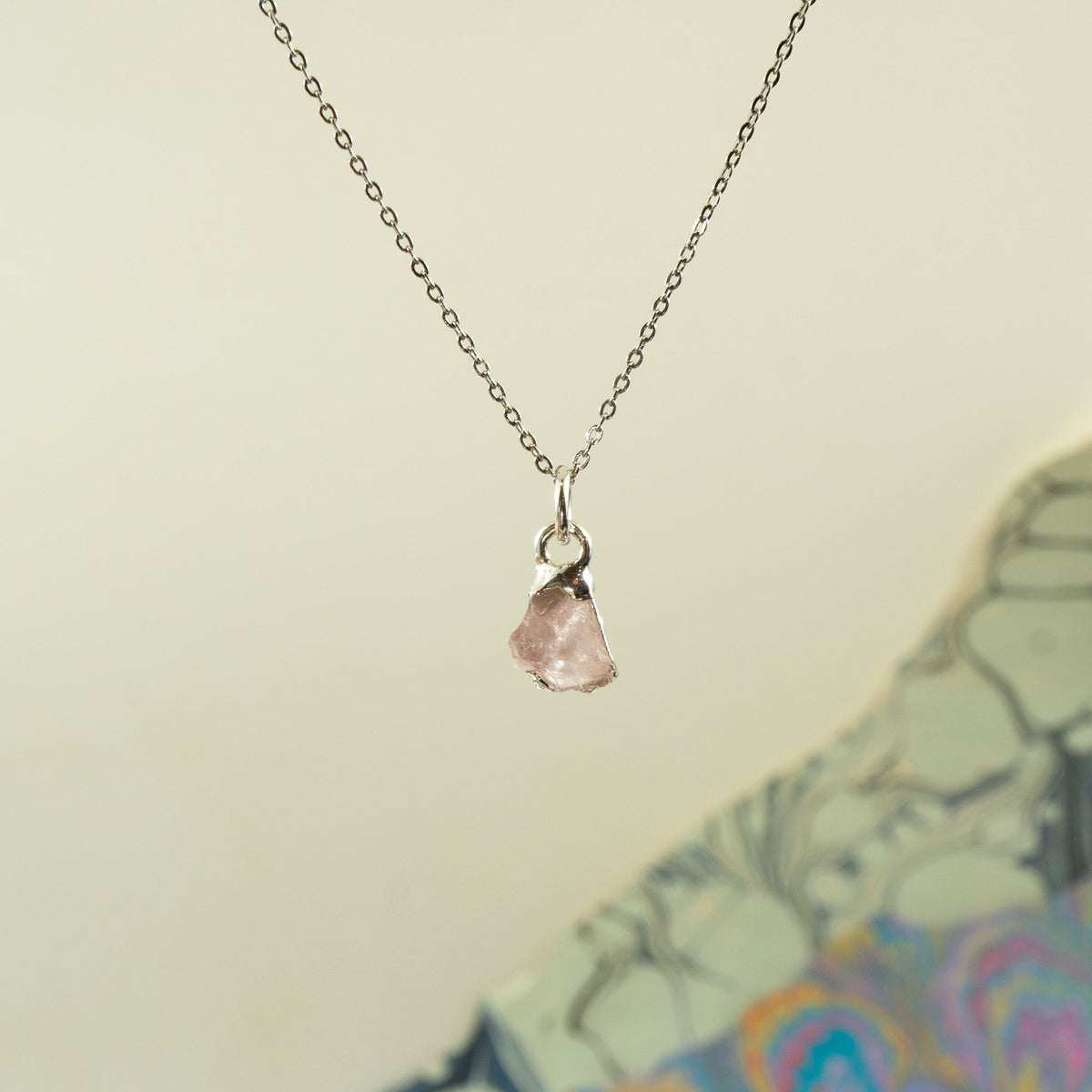 A delicate silver chain necklace with a small, rough-cut rose quartz stone pendant,