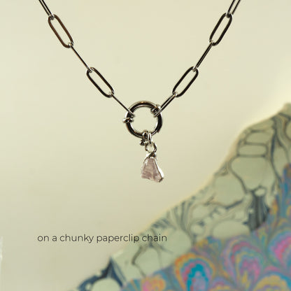A silver-toned necklace with chunky paperclip links and a small dangling faceted rose quartz crystal charm