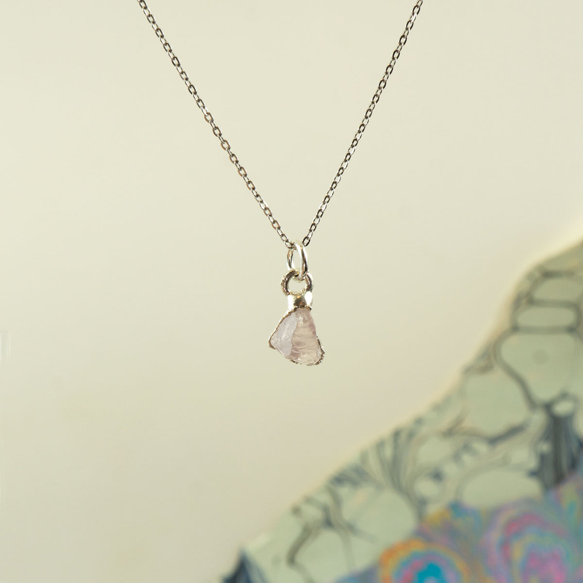 A delicate silver chain necklace with a small, irregular pale rose quartz gemstone pendant