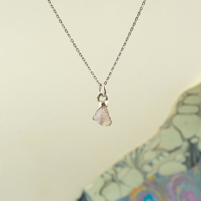A delicate silver chain necklace with a small, irregular pale rose quartz gemstone pendant