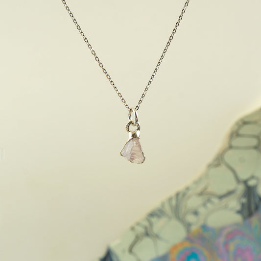 A delicate silver chain necklace with a small, irregular pale rose quartz gemstone pendant