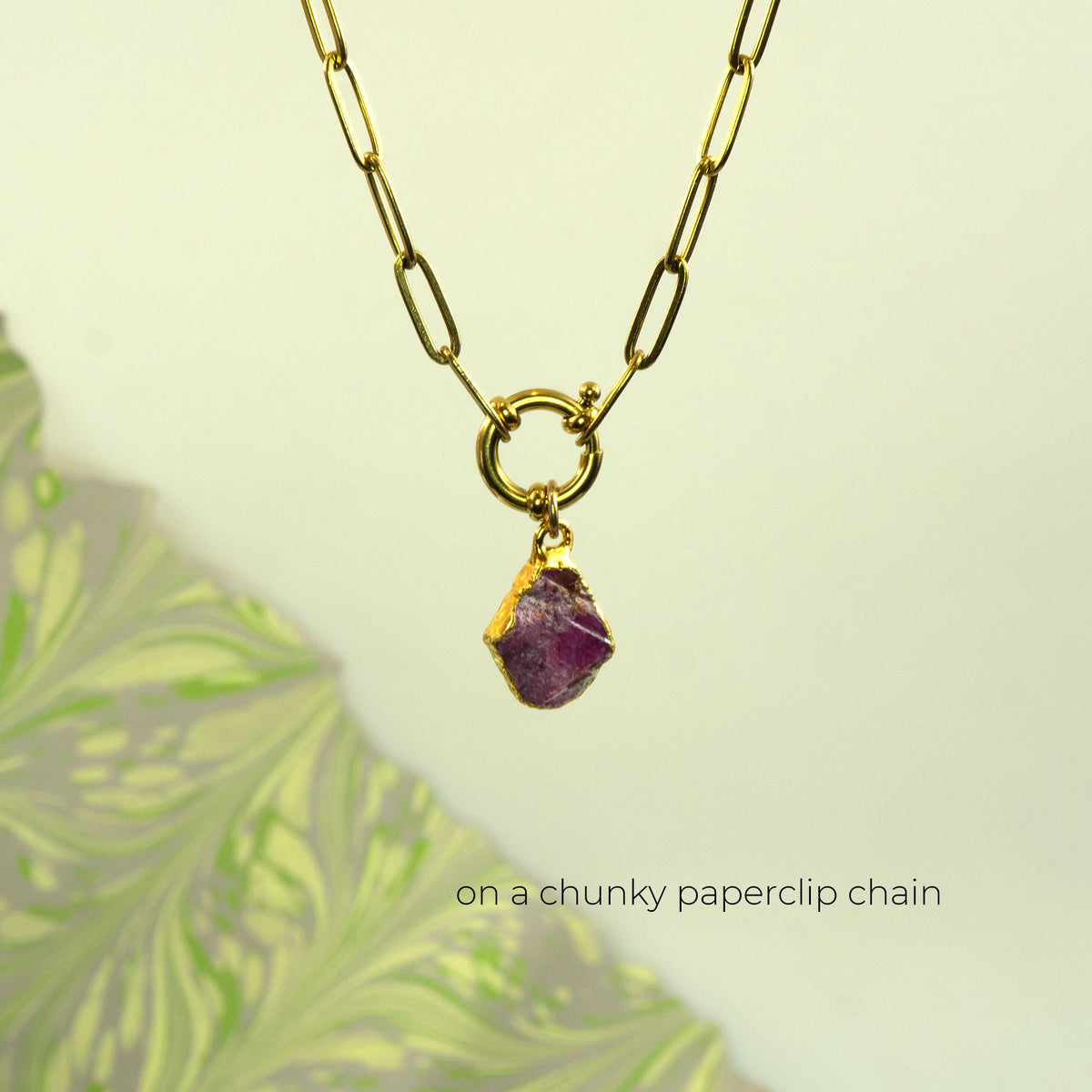 A gold paperclip chain necklace with a raw ruby gemstone pendant