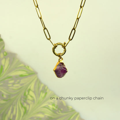 A gold paperclip chain necklace with a raw ruby gemstone pendant