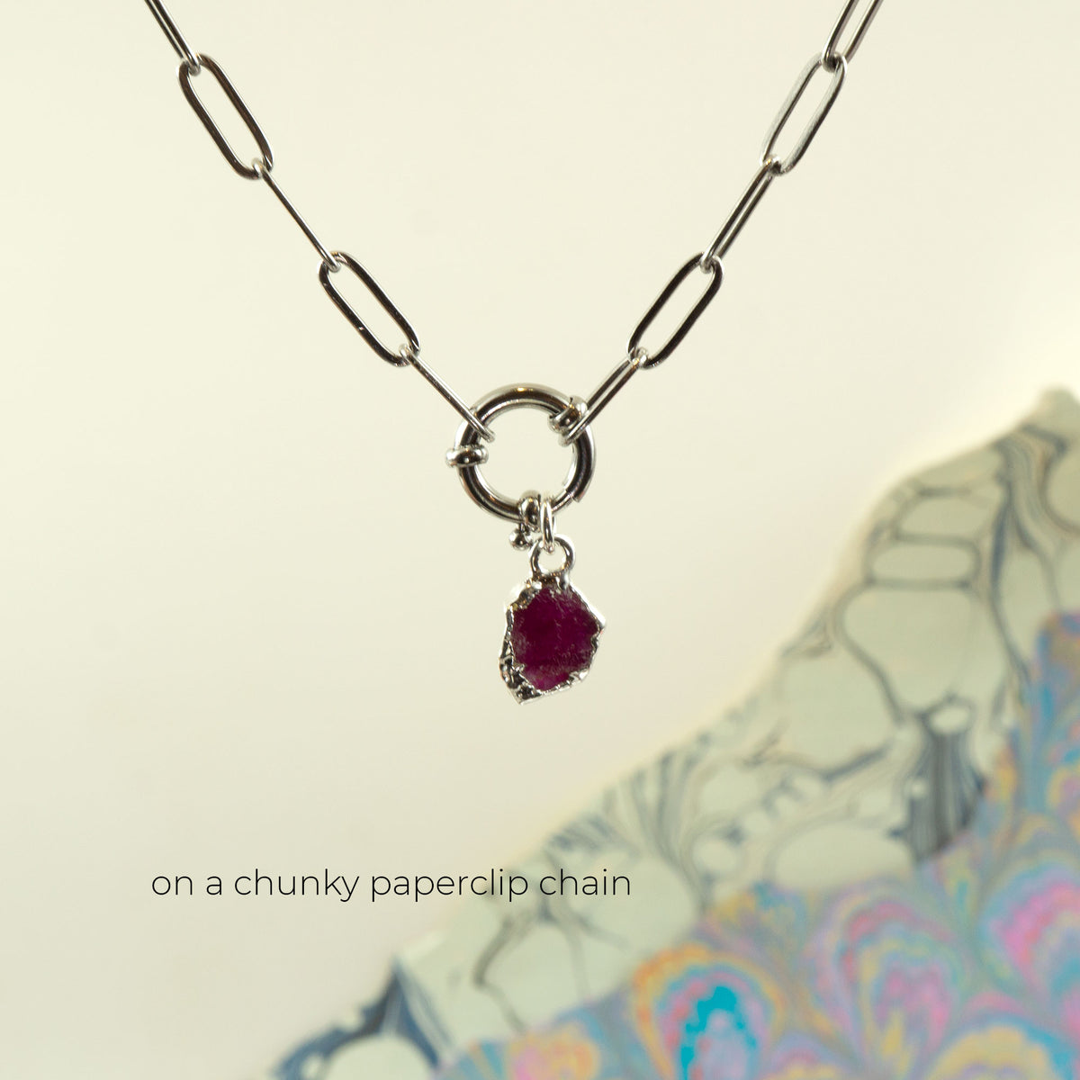 A silver paperclip chain necklace with a ring clasp and a small irregular dark ruby gemstone pendant