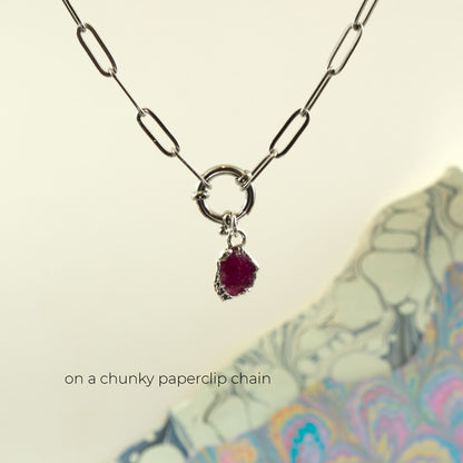 A silver paperclip chain necklace with a ring clasp and a small irregular dark ruby gemstone pendant