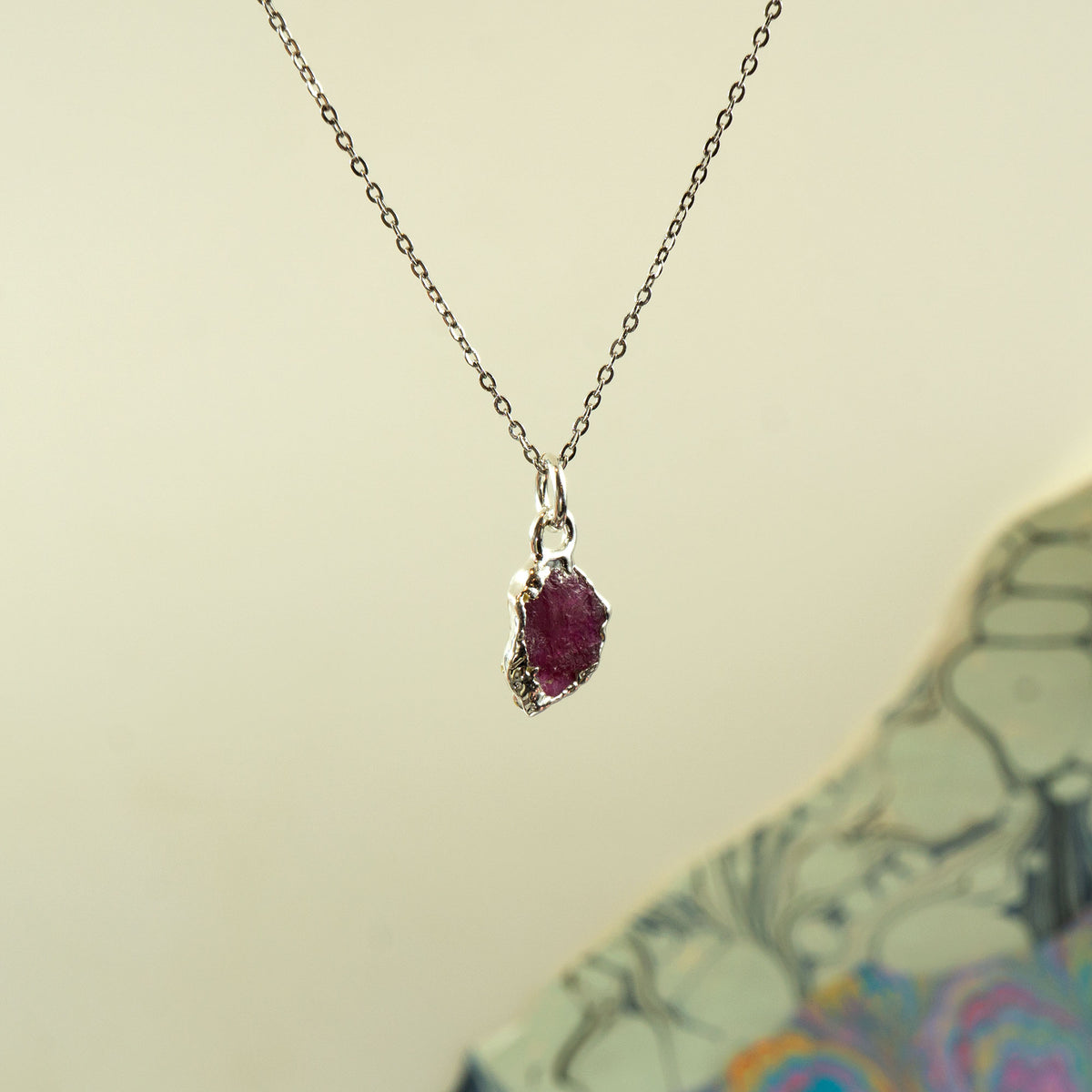 A silver chain necklace with a small, rough-cut ruby-red gemstone pendant,