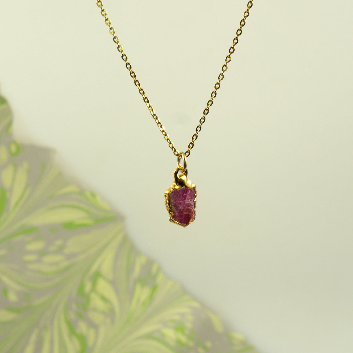 A gold chain necklace with a small, rough-cut ruby gemstone pendant.