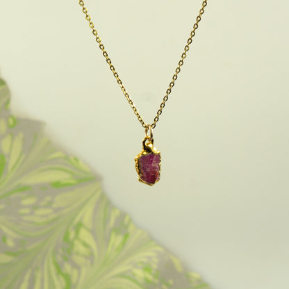 A gold chain necklace with a small, rough-cut ruby gemstone pendant.