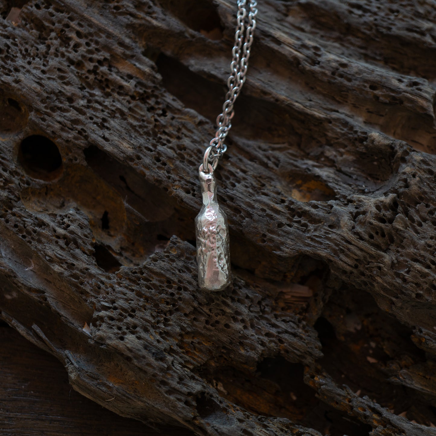 Silver bottle of beer pendant on a chain against a textured brown background