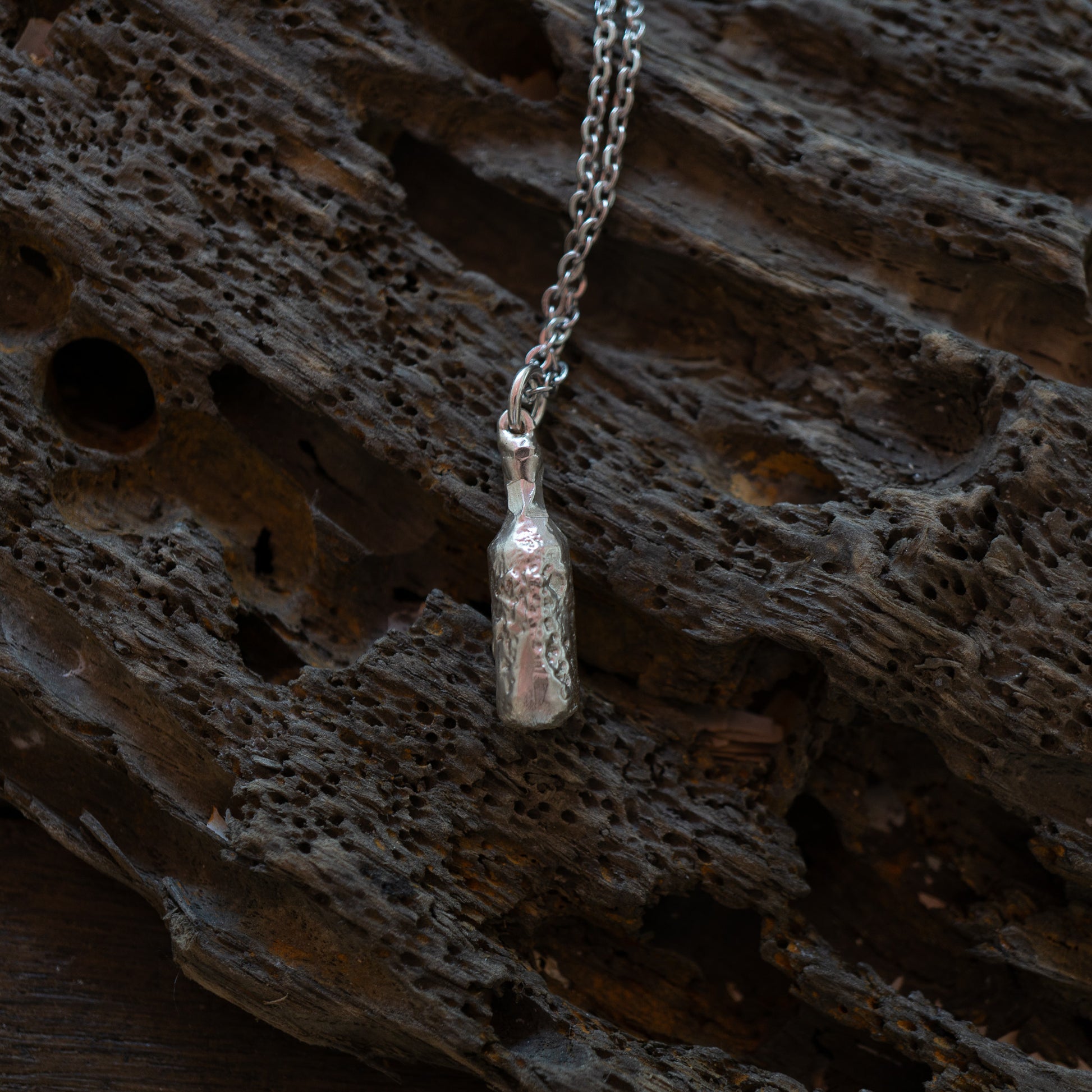 Silver bottle of beer pendant on a chain against a textured brown background