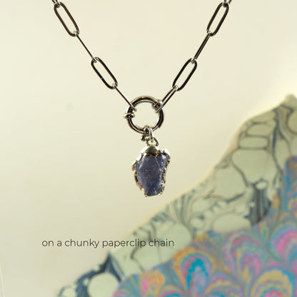 irregular shaped blue-purple raw tanzanite gemstone pendant embezzled in solid silver, on a chunky silver paperclip chain.