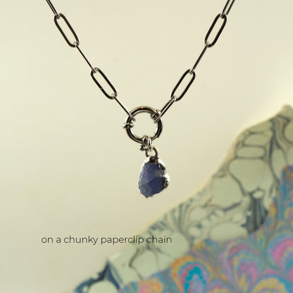 A silver paperclip chain necklace with a ring clasp and a small irregular blue tanzanite gemstone pendant