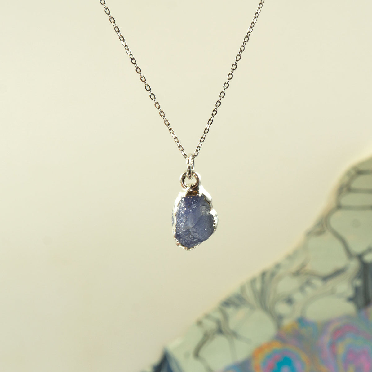 A silver chain necklace with a raw, irregular-shaped blue tanzanite gemstone pendant