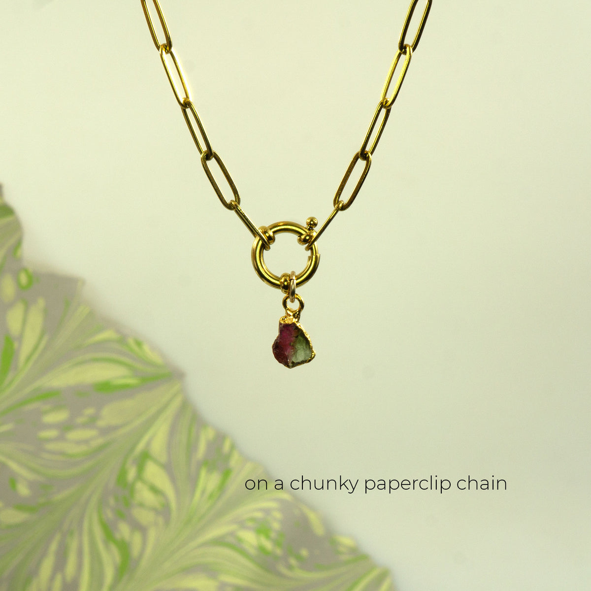 A gold paperclip chain necklace with a toggle clasp and a small dangling greenish-pink Watermelon Tourmaline gemstone pendant