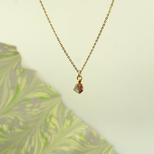 A delicate gold chain necklace with a small, irregularly shaped pendant featuring a pinkish-red and green iridescent Watermelon Tourmaline gemstone.