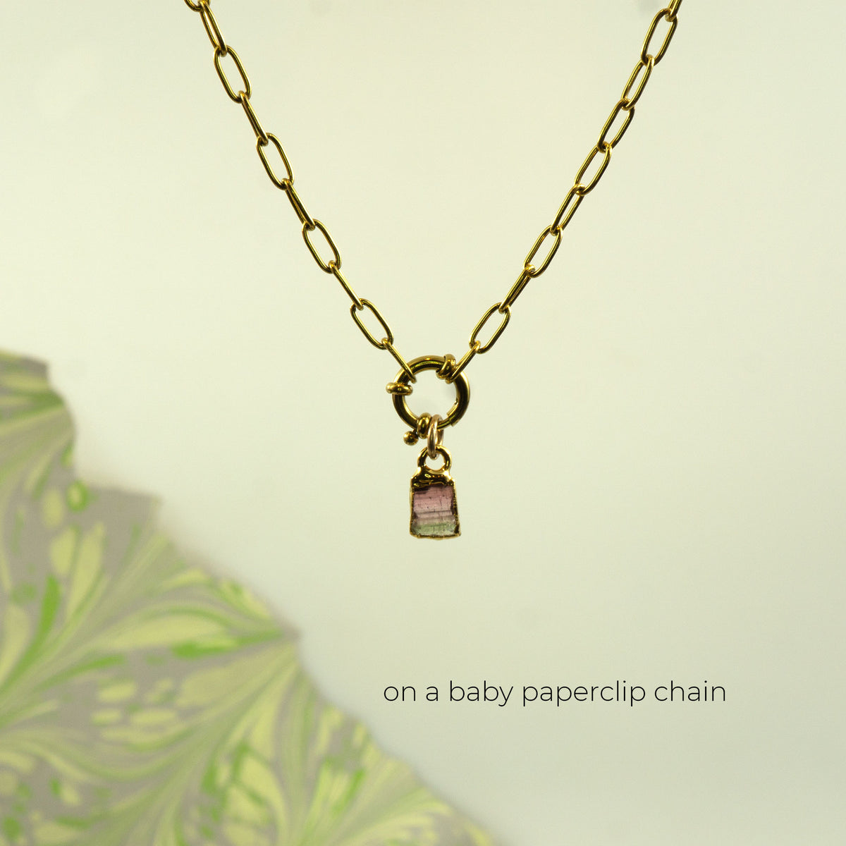 A gold paperclip chain necklace with a small charm featuring pink and green striped Watermelon Tourmaline crystal