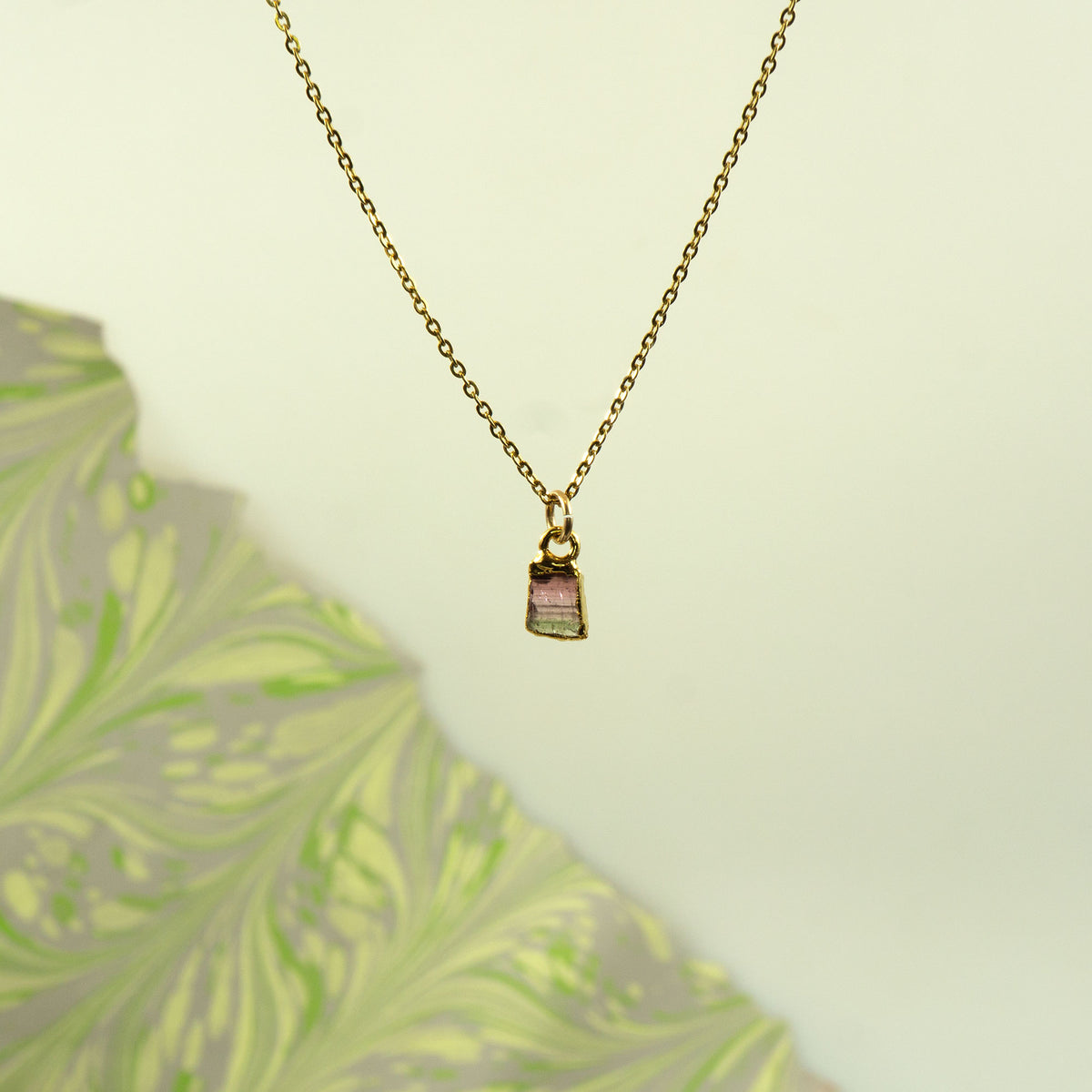 A delicate gold chain necklace with a small rectangular pendant featuring a pink and green striped Watermelon Tourmaline gemstone.